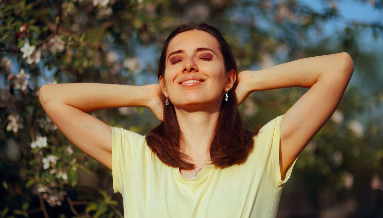 Frau hält Gesicht und Arme der Sonne entgegen. 