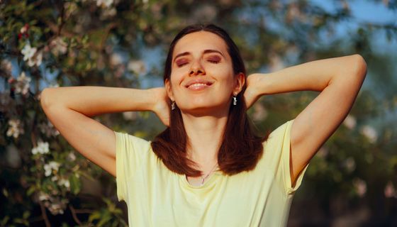 Frau hält Gesicht und Arme der Sonne entgegen.
