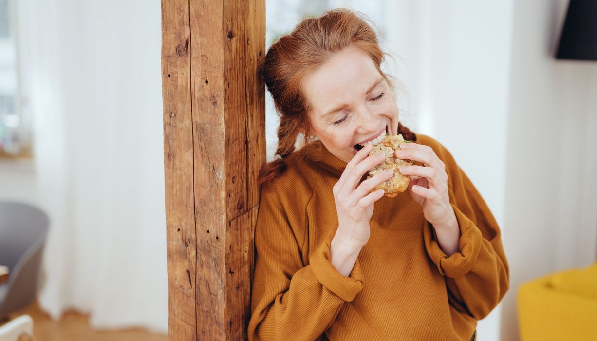 Junge Frau beißt in ein Brötchen.