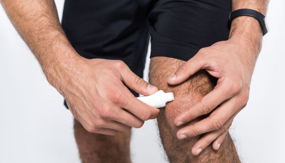 Ein Mann in Sportkleidung schmiert sich eine Salbe auf sein Knie.