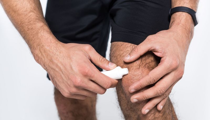Ein Mann in Sportkleidung schmiert sich eine Salbe auf sein Knie.