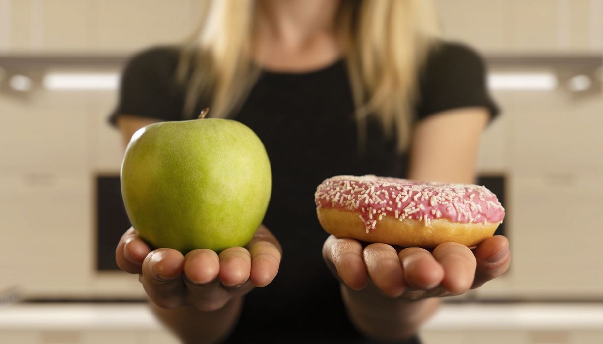 Frau, hält einen Apfel und einen Donut in der Hand.