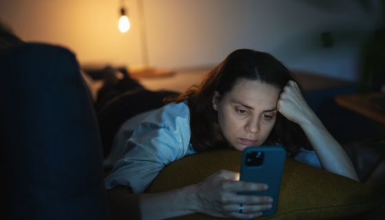 Frau, liegt im Bett und schaut auf ihr Smartphone.