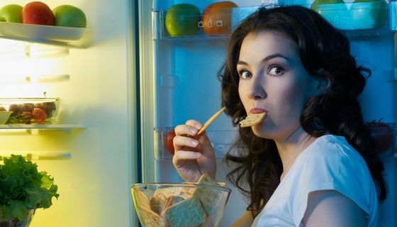 Junge Frau nachts am Kühlschrank und isst einen Snack