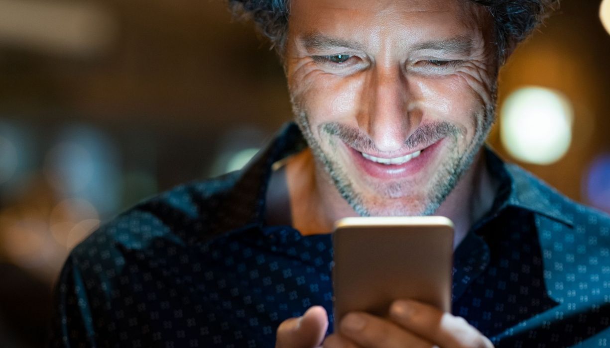 Junger Mann schaut auf sein Handy, glücklich.