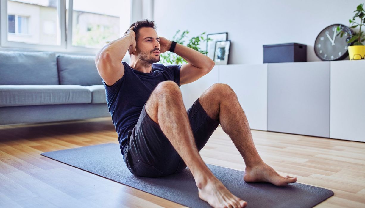 Mann, macht Sit-ups im Wohnzimmer.