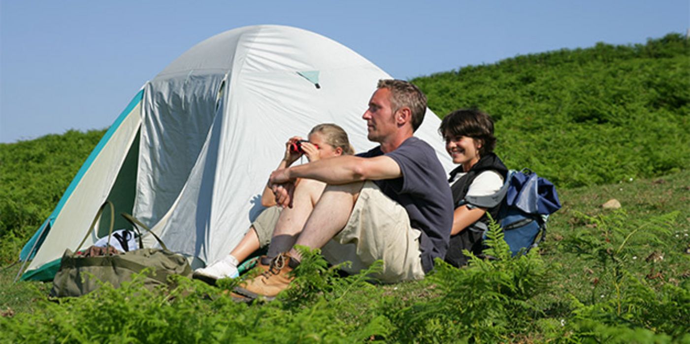 Vater, Mutter, Kind (Mädchen, ca. 10 )mit Fernglas, sitzen vor Igluzelt am Berghang zwischen Farnkraut