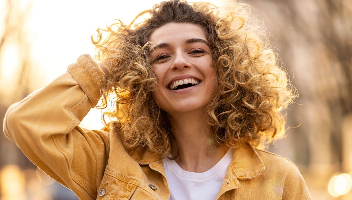 Junge Frau mit Locken, lacht in die Kamera.