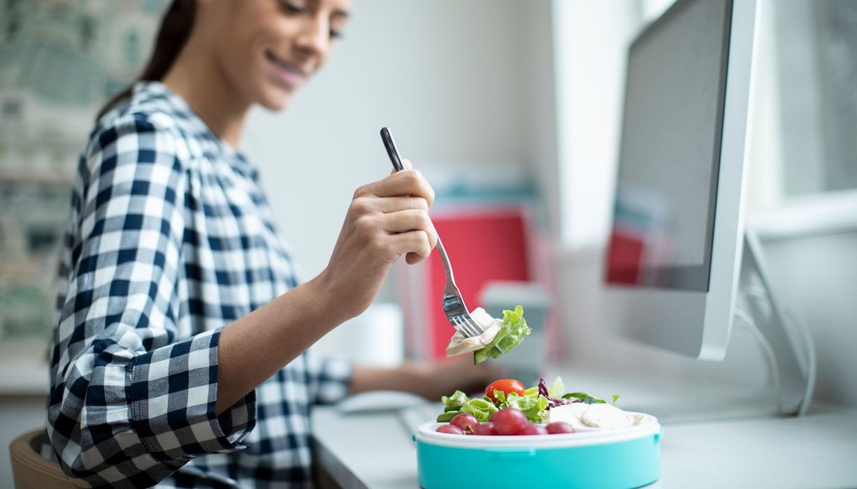 Frau, isst an ihrem Schreibtisch einen Salat.