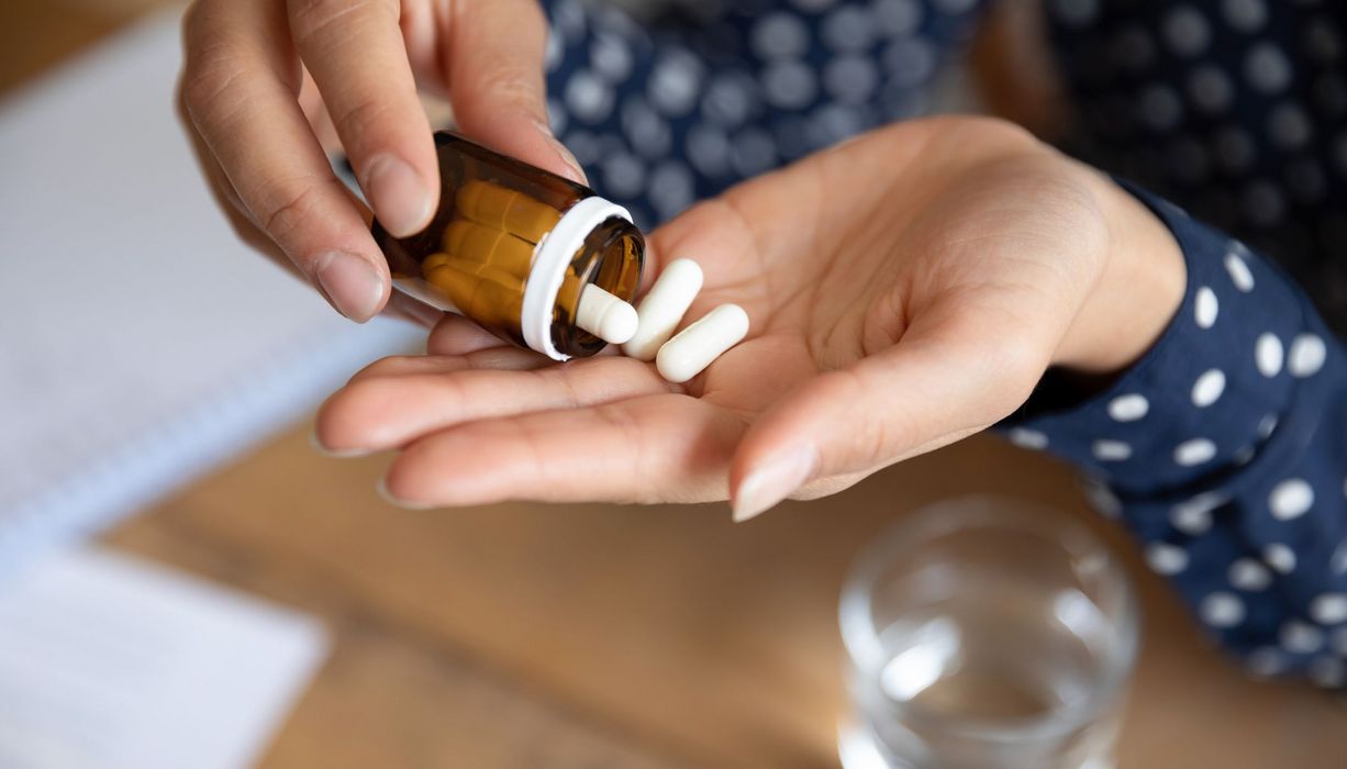 Frau, schüttet Tabletten aus einer Packung heraus.