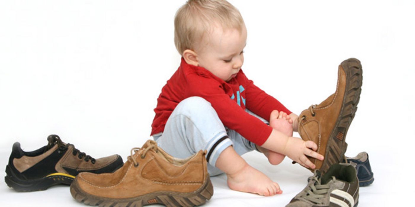 Kind spielt mit großen Schuhen.