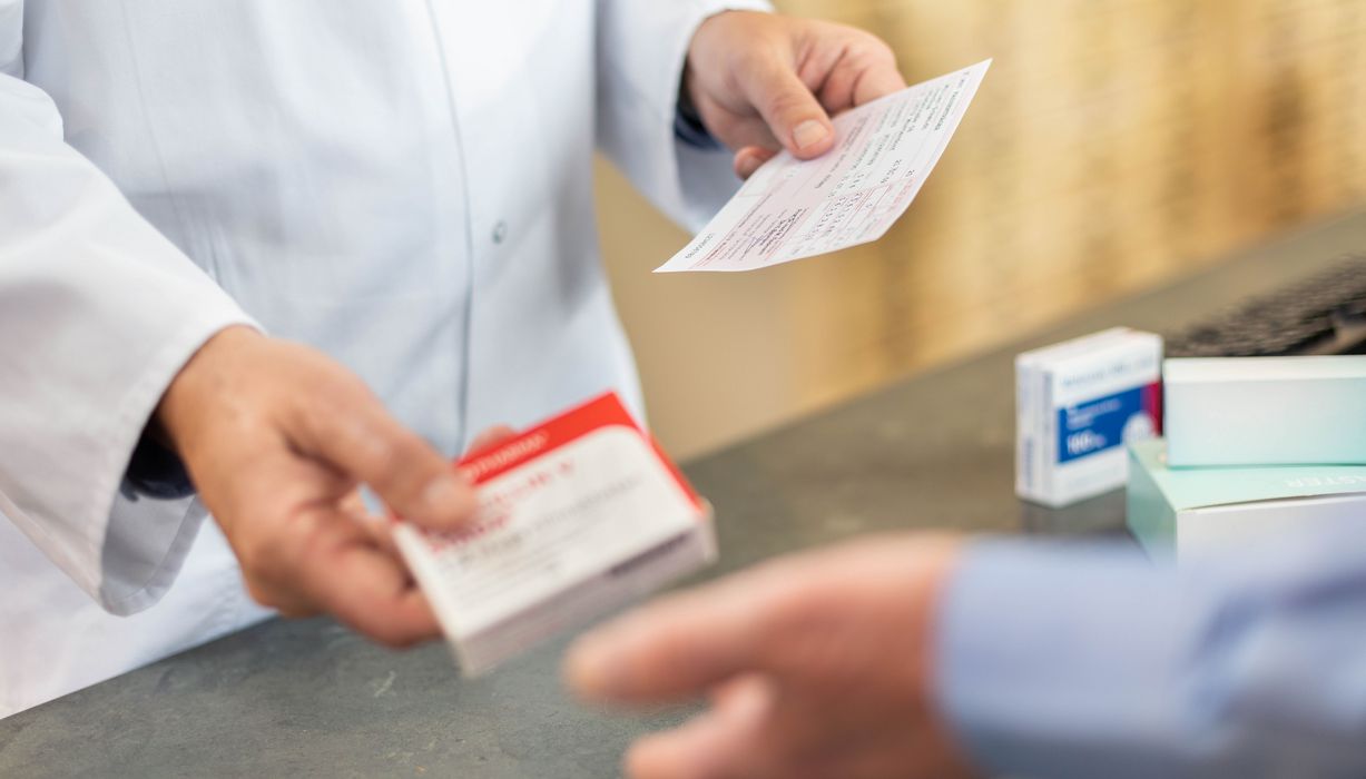 Patient tauscht ein rosa Rezept in der Apotheke gegen ein Medikament aus.