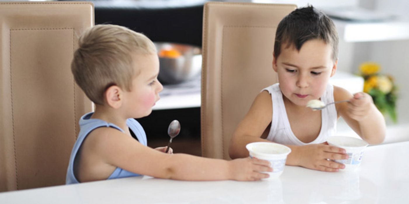 Zwei kleine Jungen essen Joghurt, der eine bietet dem anderen seinen Becher an