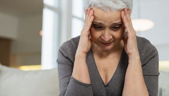Ältere Frau mit kurzen, grauen Haaren, hält sich den Kopf.