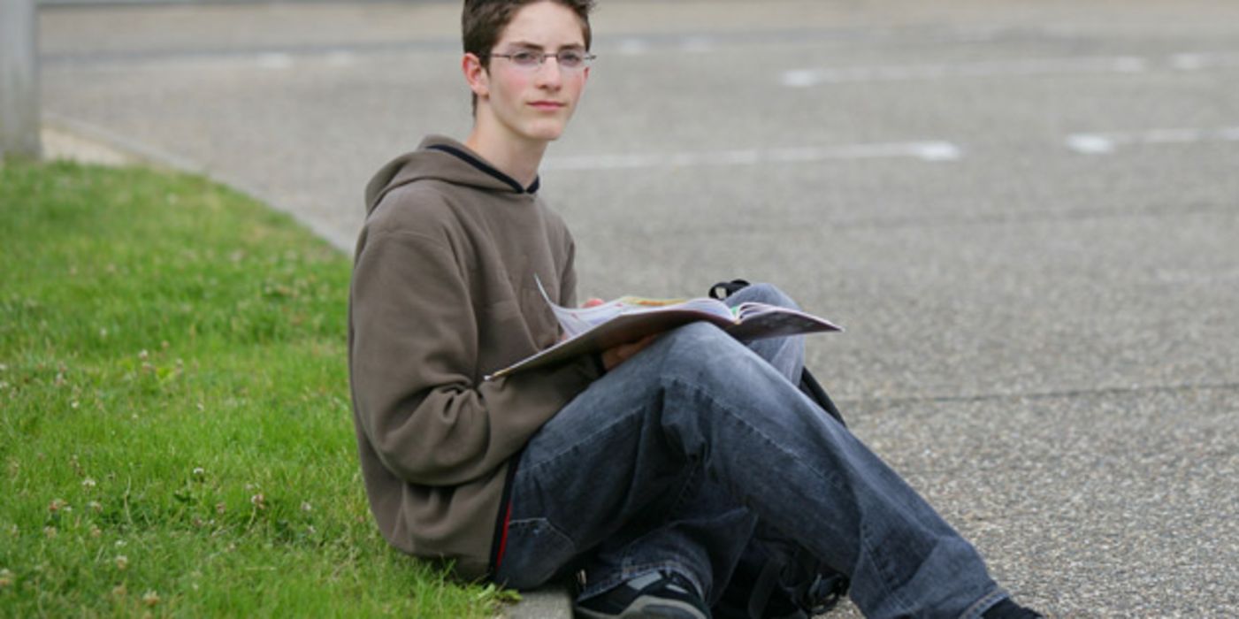 Junge sitzt auf Schulhof.