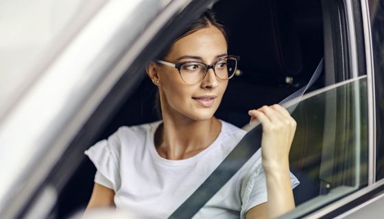 Frau, sitzt im Auto und schnallt sich an.