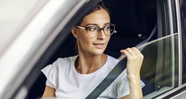 Frau, sitzt im Auto und schnallt sich an.