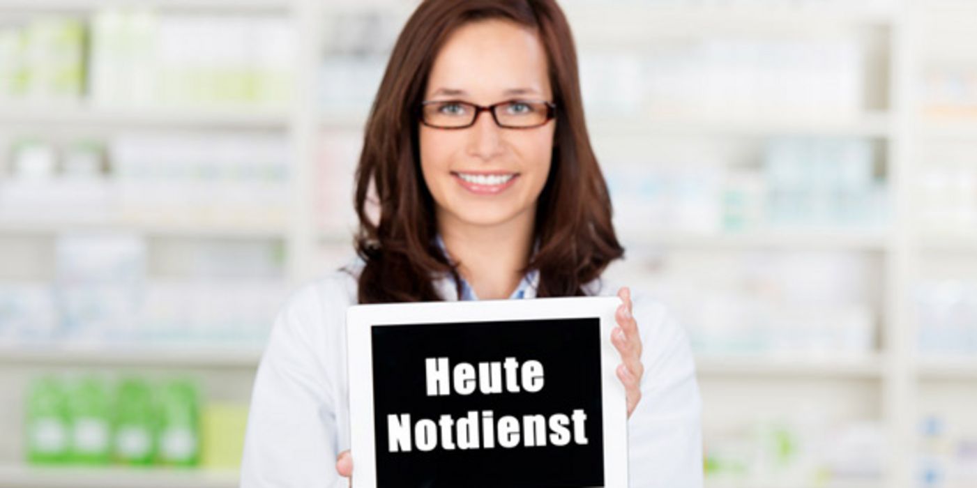 Apothekerin hält ein Schild mit der Aufschrift "Heute Notdienst" in die Kamera