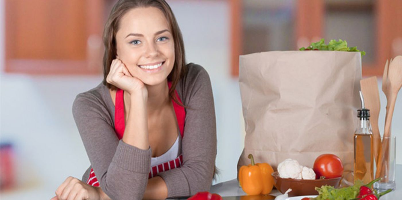 Junge Frau in der Küche, rotweiße Schürze, beim Kochen mit Gemüse