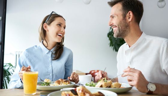 Paar sitzt am Tisch in einer Wohnung und isst gemeinsam eine warme Mahlzeit