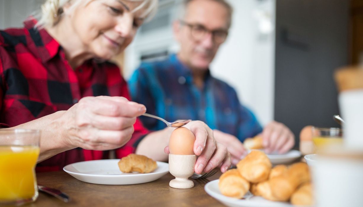 Frau, klopft auf ihr Frühstücksei mit einem Löffel.