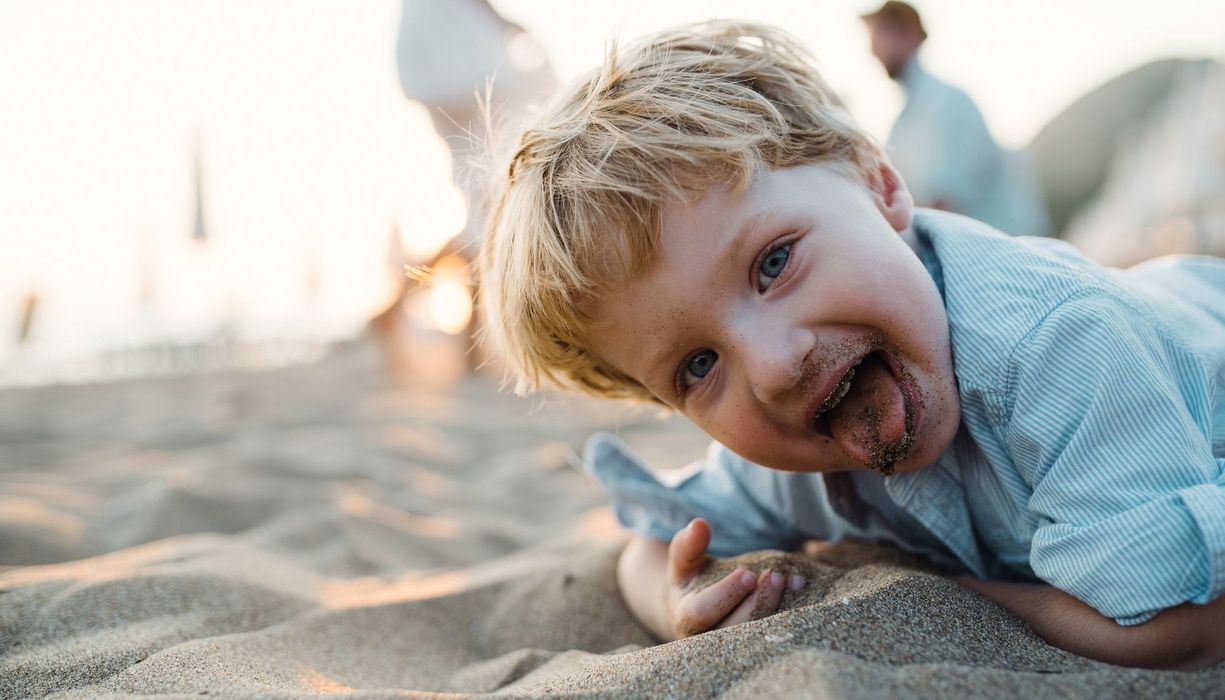 Kind, steckt sich Sand in den Mund.