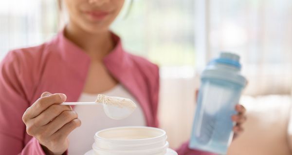 Junges Mädchen, nimmt einen Löffel Proteinpulver aus einer Packung.