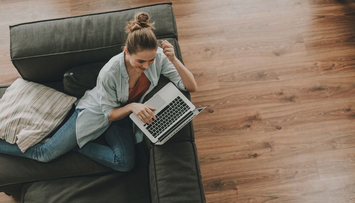 Junge Frau, sitzt mit Laptop auf der Couch.