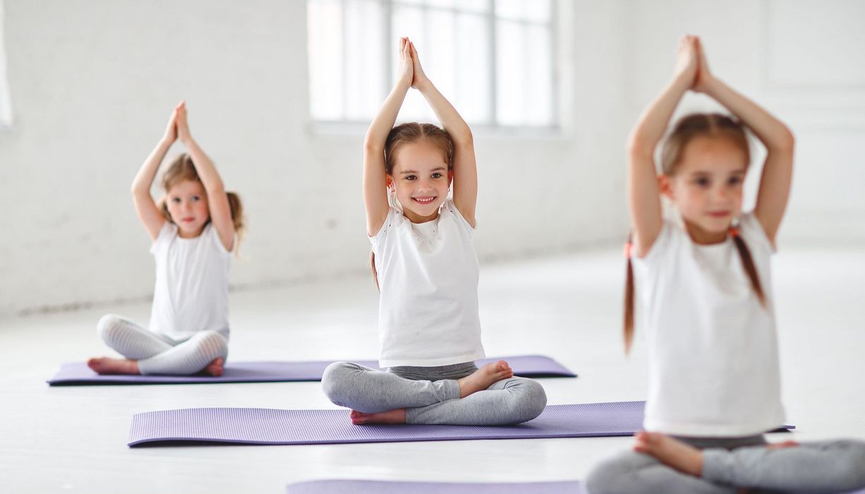 Drei Kinder, je auf einer Yogamatte.