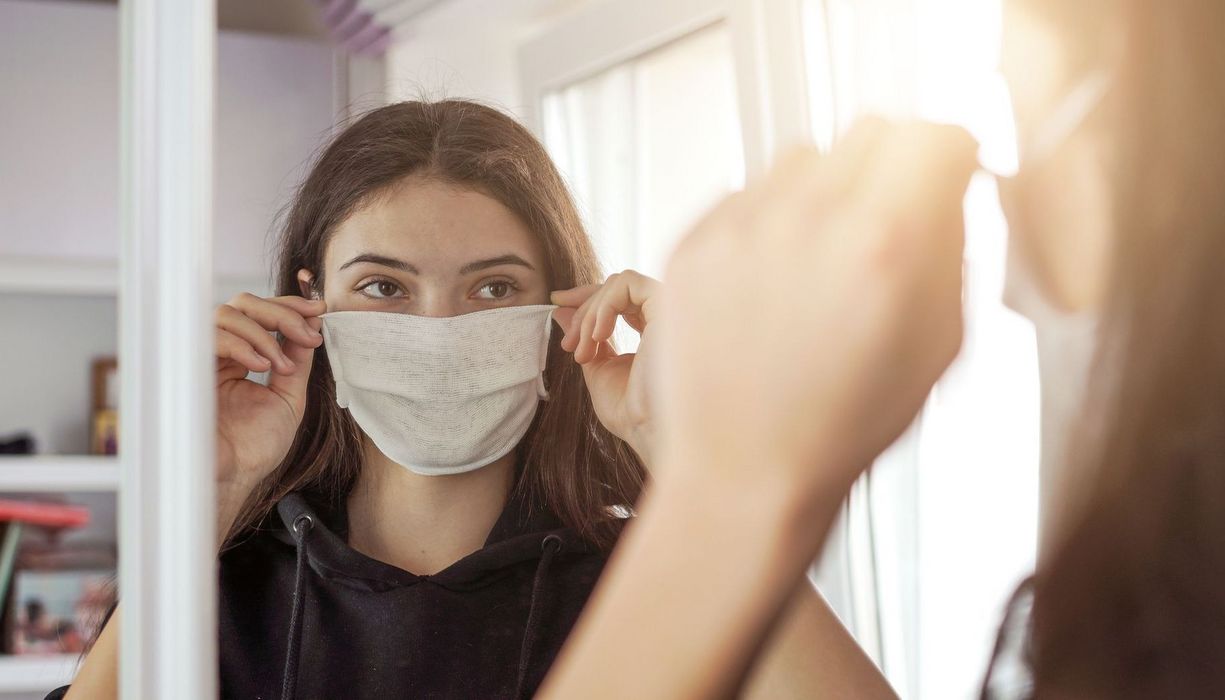 Junges Mädchen, steht vor einem Spiegel und setzt sich eine Maske auf.