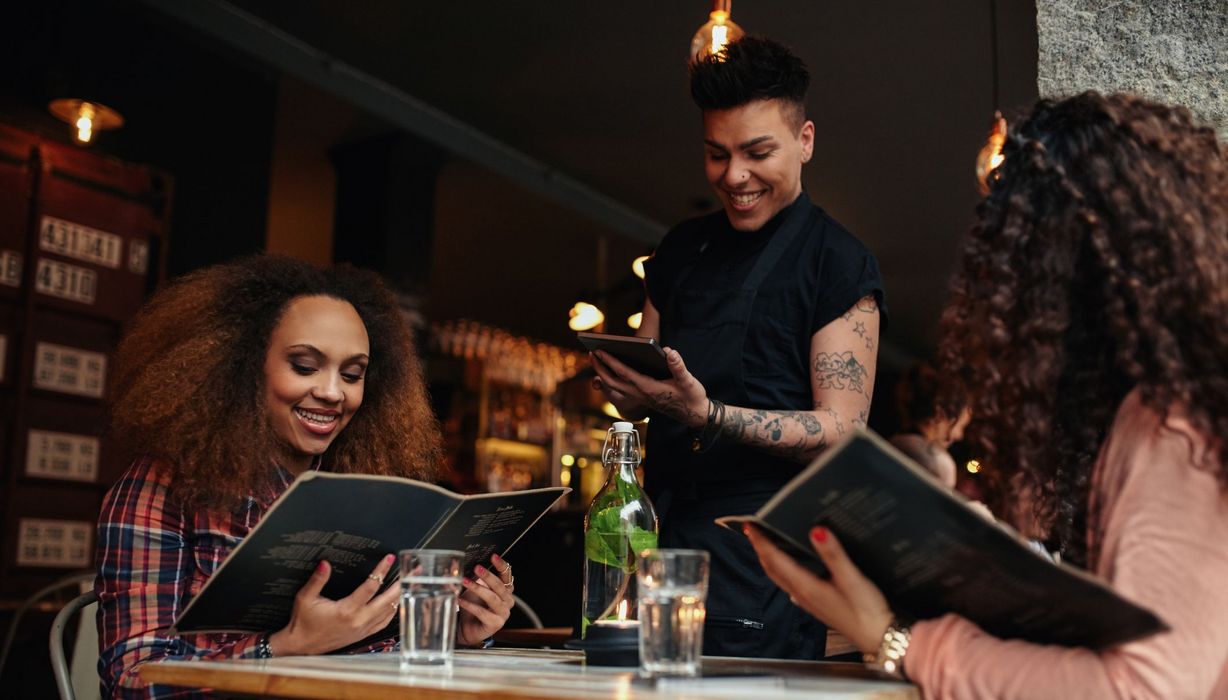 Zwei Frauen im Restaurant, schauen sich Speisekarten an.