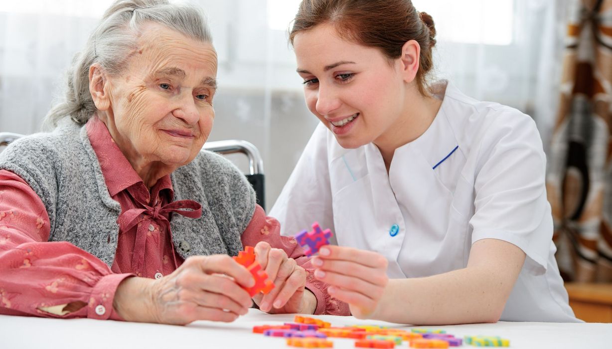 Junge Pflegerin, beschäftigt sich mit Demenz-Patienten und großen Puzzel-Teilen.