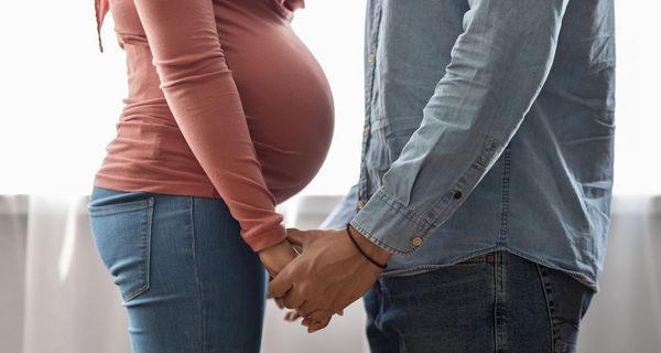 Schwangere Frau, steht vor einem Mann, beide halten sich an der Hand.