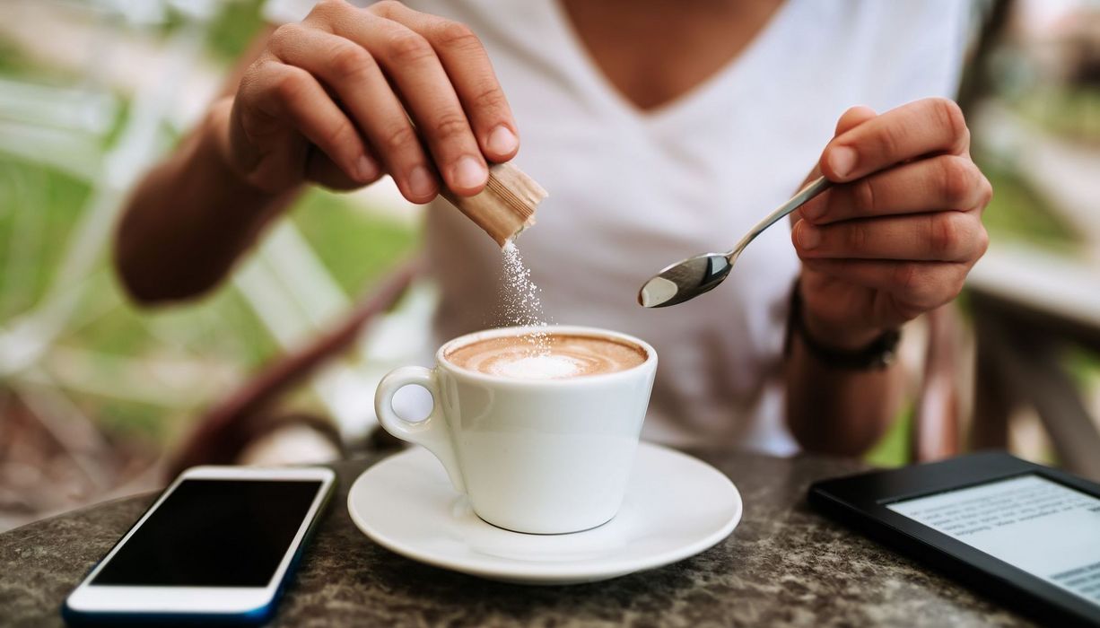 Frau, schüttet Zucker in ihren Kaffee.