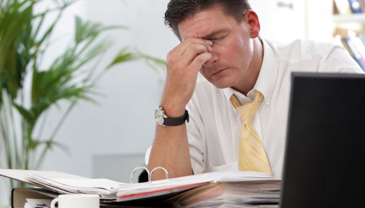 Ein junger Mann sitzt im Büro und schlägt die Hände über dem Kopf zusammen.