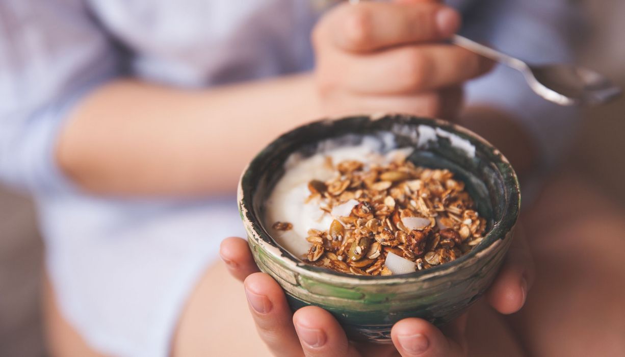 Frau, hält eine kleine Schale mit Müsli in der Hand.