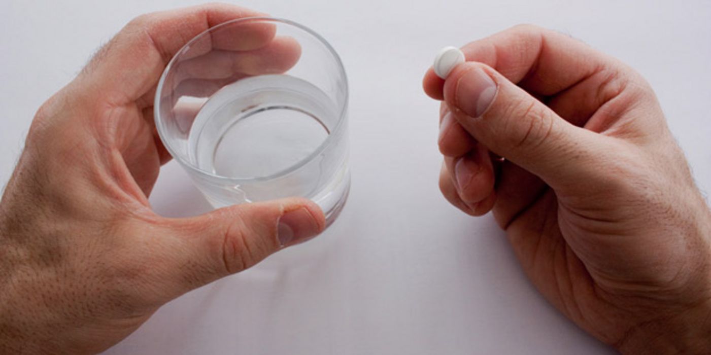 Eine Hand hält ein Glas mit Wasser, die andere eine weiße Tablette