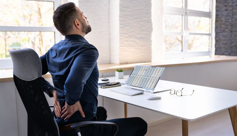 Mann am Schreibtisch hält sich den Rücken.
