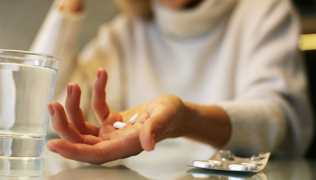 Frau, hält mehrere Tabletten in einer Hand, daneben ein Glas Wasser.