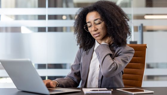 Junge Frau im Büro legt sich die Hand in den Nacken.