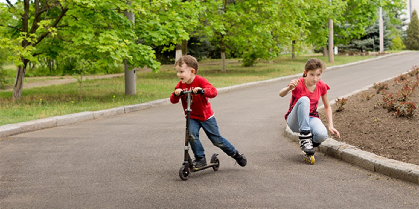 Junge ca. 5, auf Tretroller, Mädchen, ca. 9/10, auf Rollerblades auf Straße in Kurve