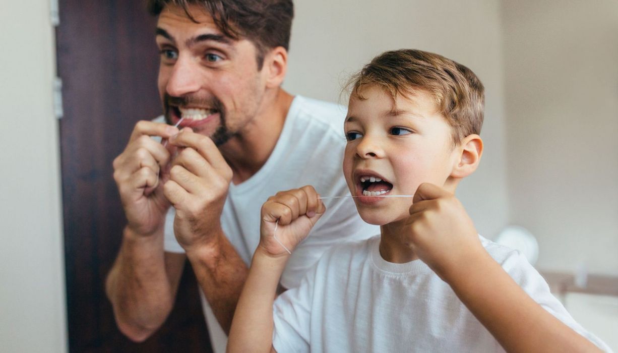 Vater und Sohn, stehen vor dem Spiegel und nutzen Zahnseide.