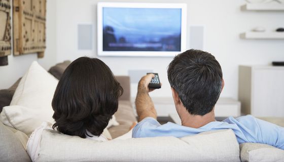 Ein Paar sitzt auf dem Sofa vom Fernseher mit dem rücken zum Betrachter.