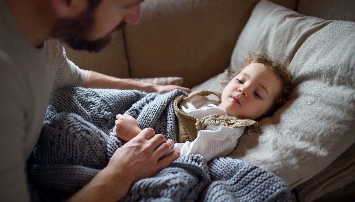 Kind, liegt im Bett, Papa sitzt daneben.