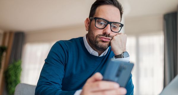 Mann, schaut gelangweilt auf sein Smartphone.