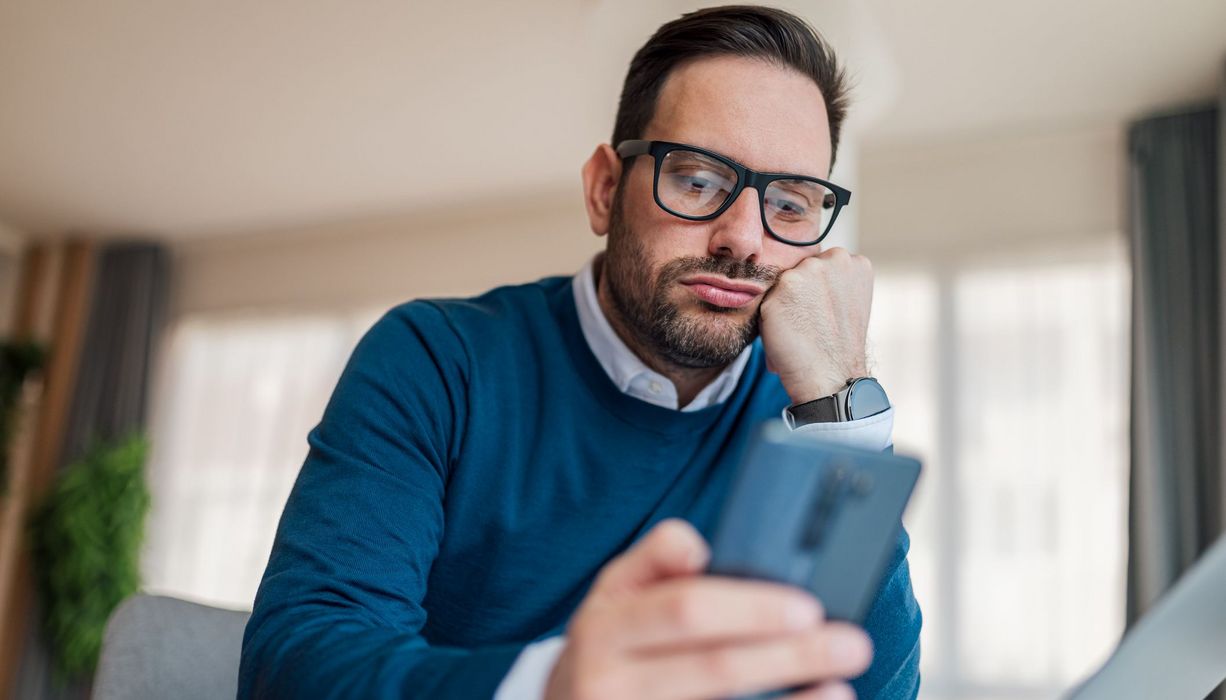 Mann, schaut gelangweilt auf sein Smartphone.