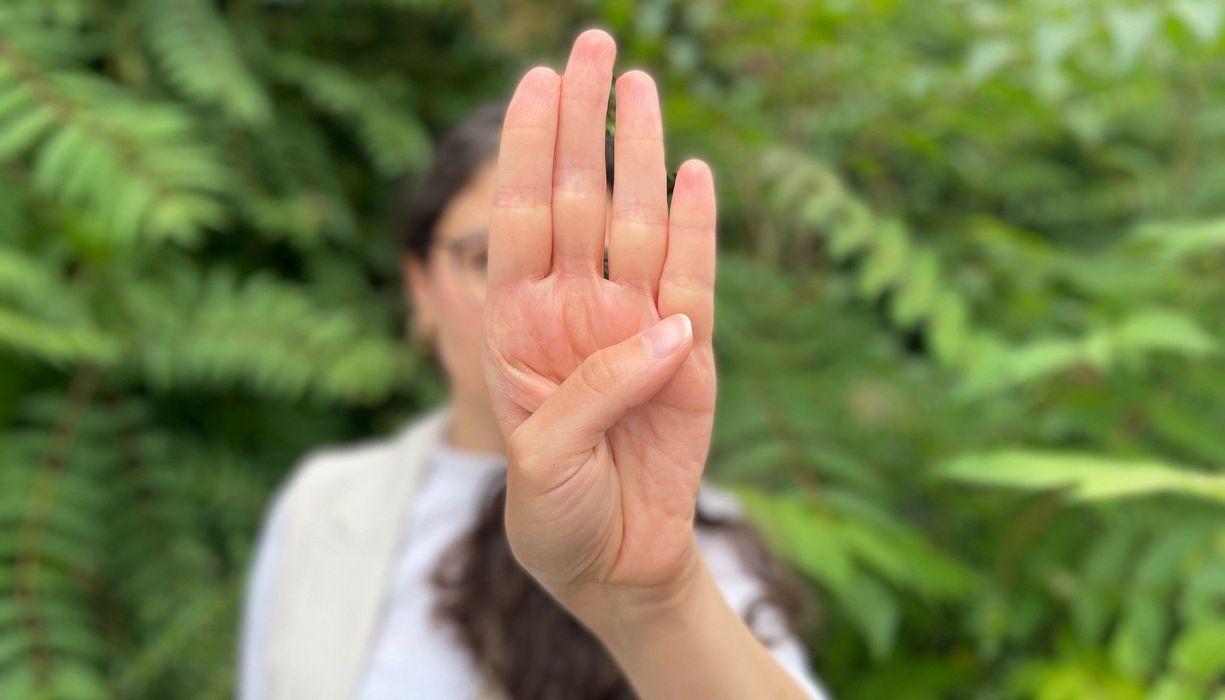 Junge Frau zeigt die Handfläche und streckt den Daumen über die Handfläche auf die gegenüberliegende Seite. 