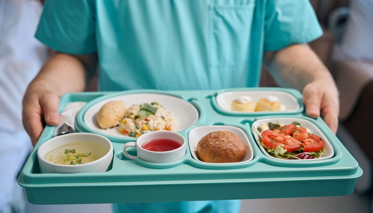 Pflegendes Personal, hält ein Tablett mit Essen in der Hand.