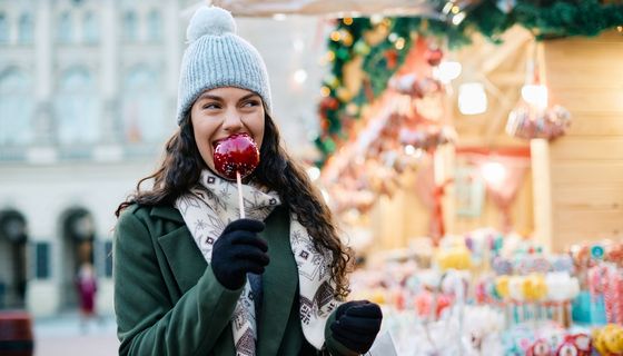 Junge Frau isst einen Bratapfel auf dem Weihnachtsmarkt.