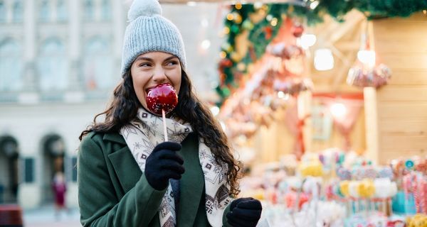 Junge Frau isst einen Bratapfel auf dem Weihnachtsmarkt.